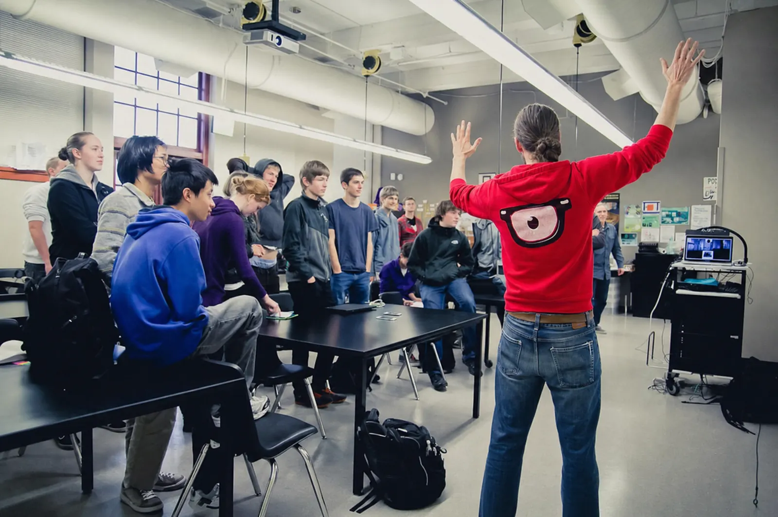 Kyle from behind, arms raised, teaching a classroom of young people
